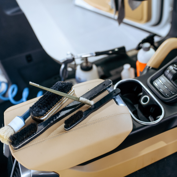 Intérieur de voiture avec brosses de finition et produits de nettoyage sur un accoudoir en cuir beige.