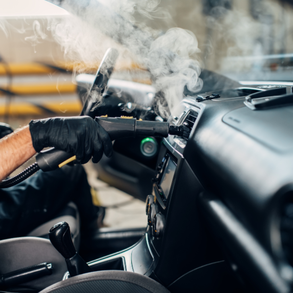 Une personne portant des gants noirs nettoie à la vapeur le tableau de bord d'une voiture.