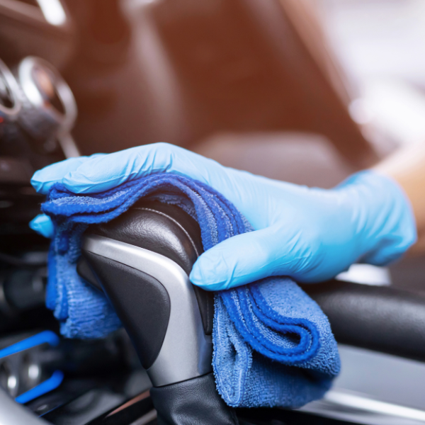 Main dans un gant bleu essuyant un levier de vitesse de voiture avec un chiffon en microfibre bleu.
