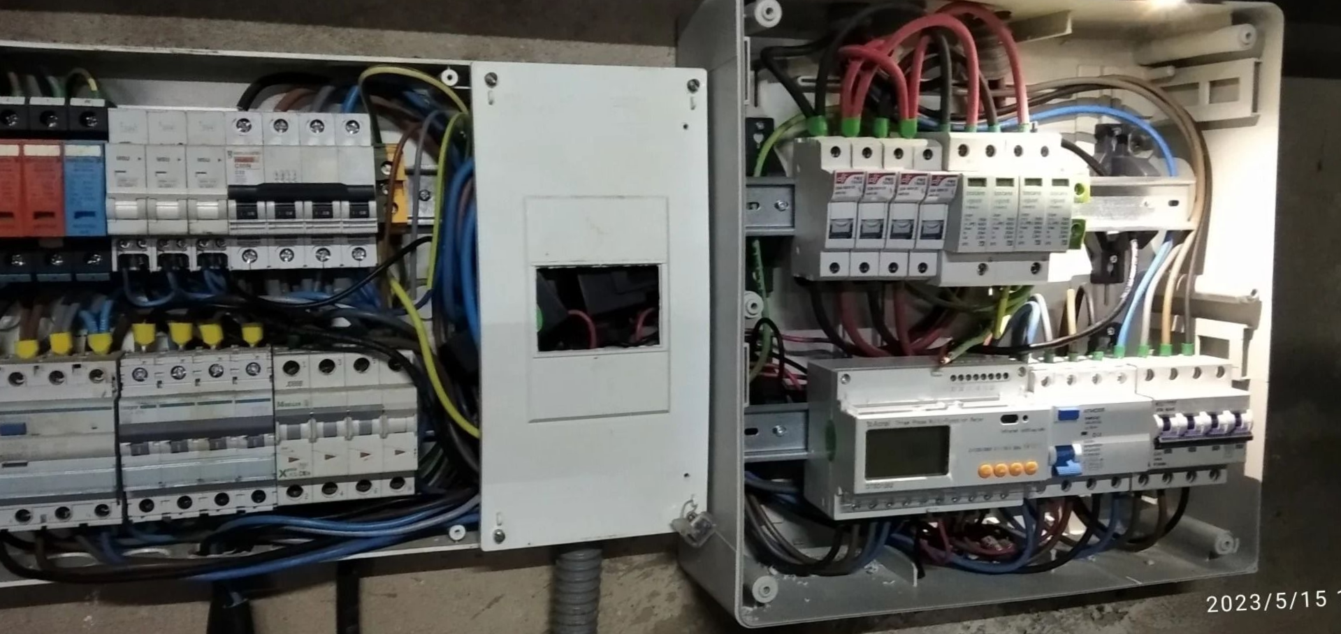 Panel de control eléctrico con disyuntores, cableado y caja de contador central montado en una pared.