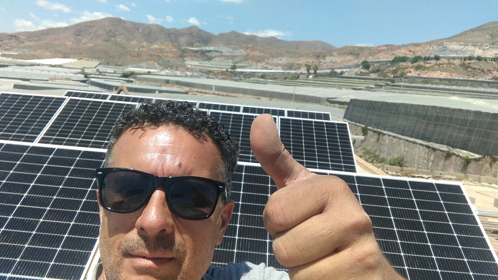 Una persona levanta el pulgar frente a unos paneles solares bajo un cielo soleado.