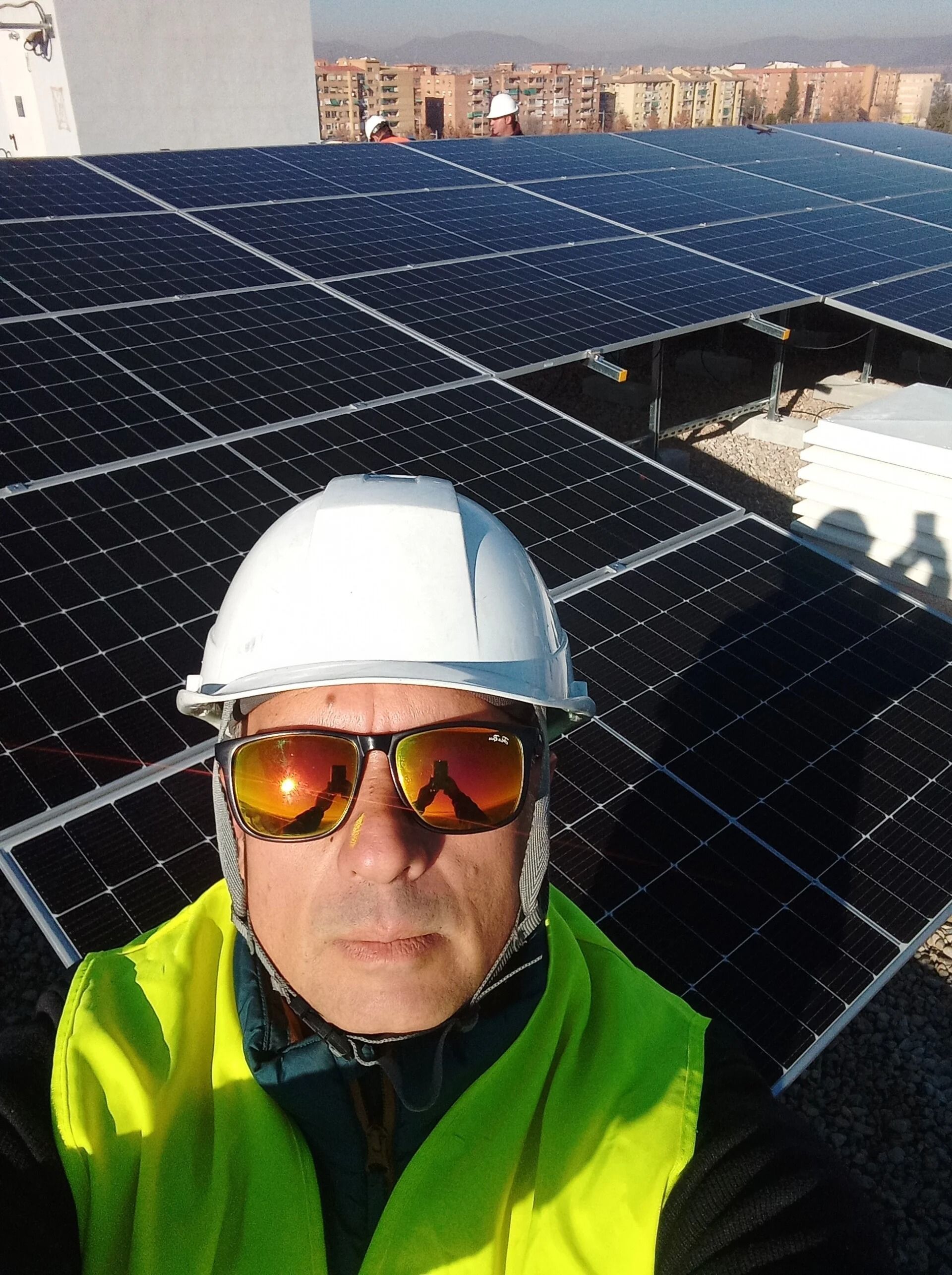 Un trabajador con casco blanco y chaqueta fluorescente en la azotea de un edificio con paneles solares