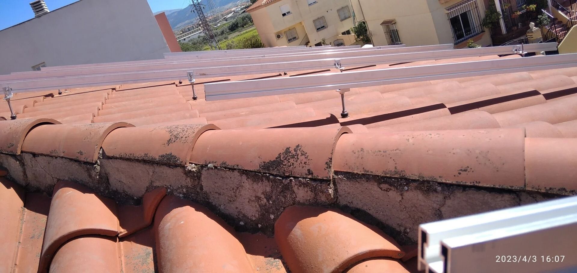 Tejas de terracota con daños visibles y grietas oscuras cerca de la cumbrera en la azotea de un edificio.