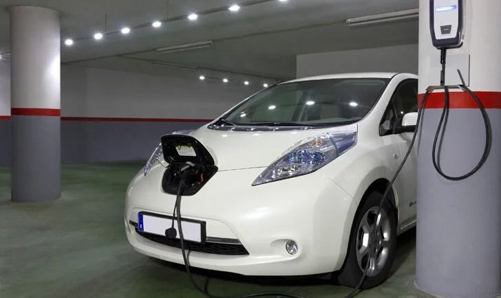 Un coche eléctrico blanco se está cargando en un garaje subterráneo, conectado a una estación de carga montada en la pared.