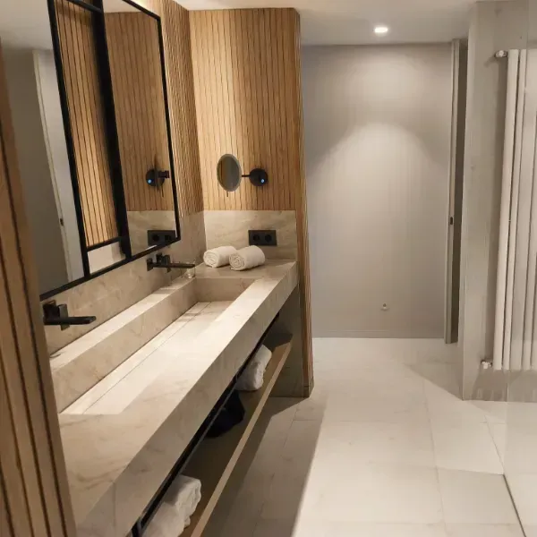 Baño moderno con lavabo doble, paredes con listones de madera, espejo grande, accesorios negros