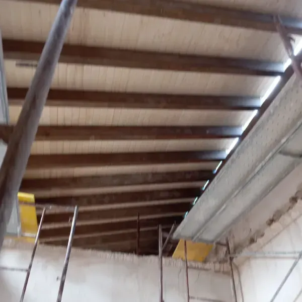 Una vista hacia arriba de un techo de madera en construcción con vigas expuestas, andamios y paneles amarillos.