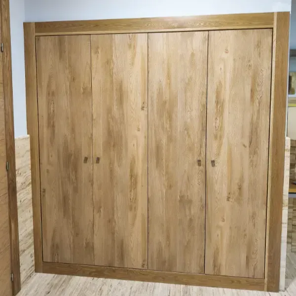 Un armario de madera de cuatro puertas con acabado en roble marrón claro y marco a juego, empotrado a ras de la pared.