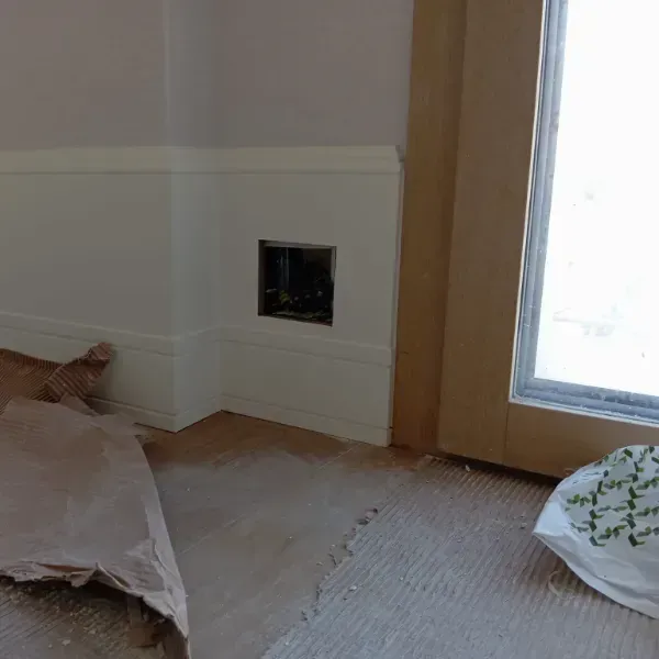 Una pared sin terminar con revestimiento blanco y una caja eléctrica expuesta cerca de una ventana