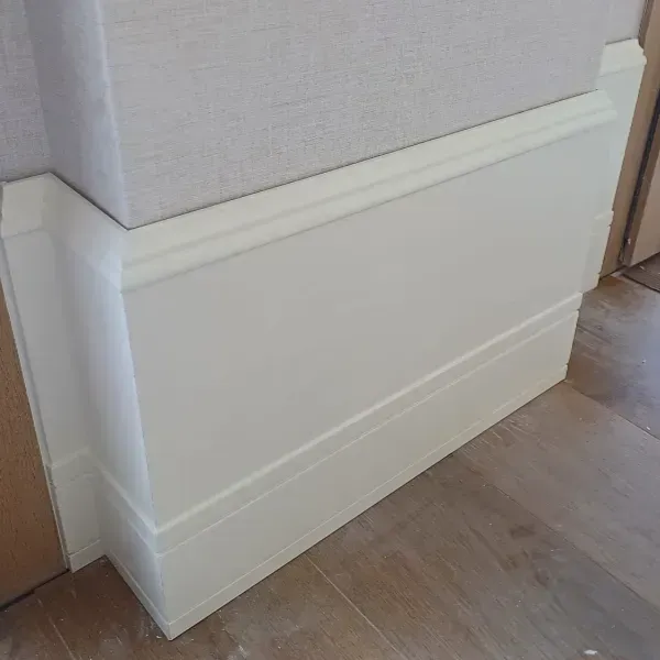 Revestimiento de madera blanco con moldura superior decorativa instalado a lo largo de una pared en una habitación