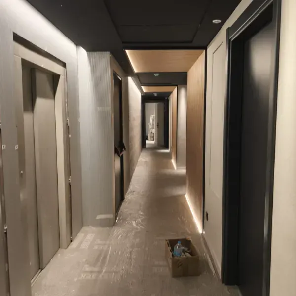 Un pasillo de hotel largo y angosto en construcción, con paredes claras, detalles oscuros en el techo