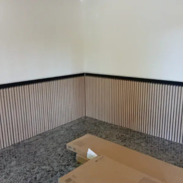 Un rincón de una habitación con paneles de listones de madera clara rematados con una moldura negra