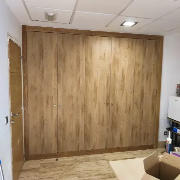 Un armario de madera de pared a pared y de suelo a techo con cuatro puertas en una habitación con suelo y paneles de techo