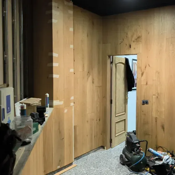 Revestimientos de madera clara sin terminar cubren una pared con una puerta y herramientas de construcción