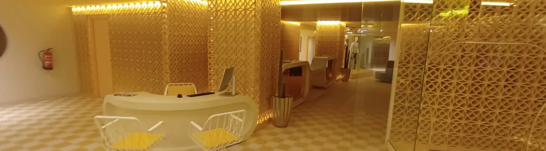 Una moderna área de recepción de spa en tonos dorados con un escritorio blanco, dos sillas.