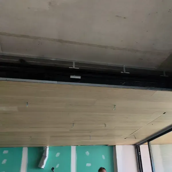 Construcción interior que muestra un techo con paneles de madera suspendido debajo de una losa de hormigón