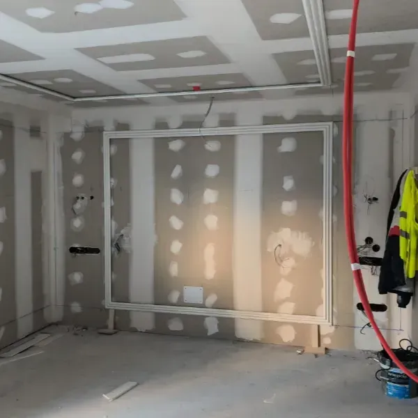Una habitación en construcción con paneles de yeso sin terminar, juntas selladas, un marco rectangular blanco en la pared