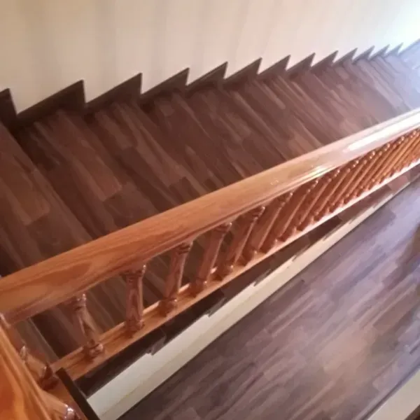 Una vista en ángulo alto de una escalera de madera con tablones de color marrón oscuro y un pasamanos de madera clara pulida