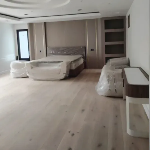 Un dormitorio moderno con suelos de madera clara, una cama con cabecero beige, estanterías empotradas y muebles