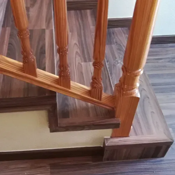 Una barandilla de escalera de madera con balaustres tallados sobre escalones cubiertos con un suelo oscuro