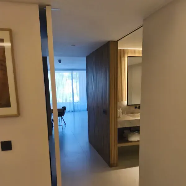 Una vista interior moderna a través de una puerta, que muestra un pasillo, un tocador de baño y una sala de estar iluminada.