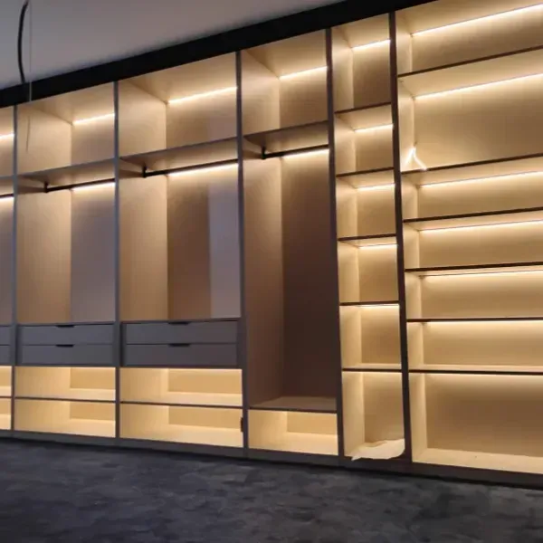 Un sistema de vestidor de madera de piso a techo con iluminación LED cálida integrada en los estantes y varios cajones.