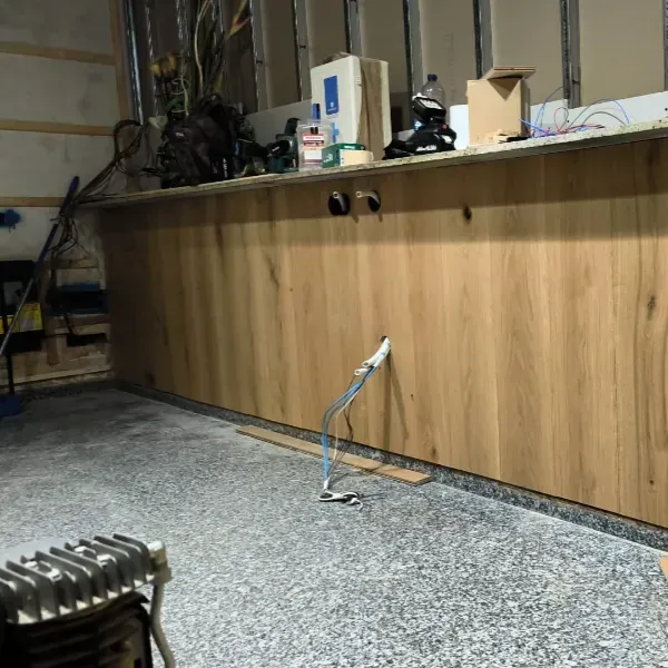 Un mostrador con frente de madera en construcción en una habitación con un piso gris moteado y vigas de pared expuestas.