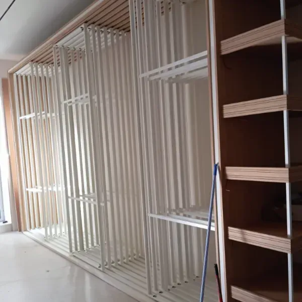 Una serie de estantes extraíbles verticales blancos junto a una estantería de madera en un espacio interior moderno.