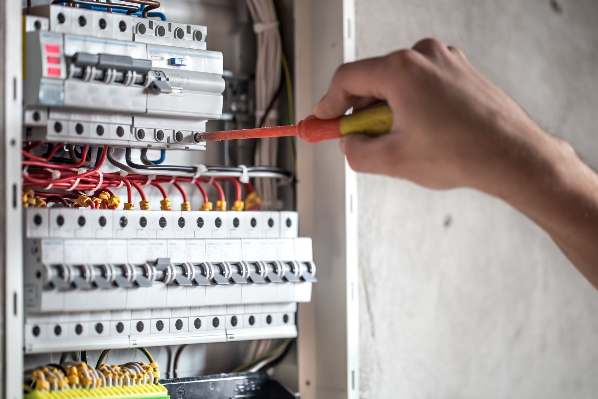 Mão usando chave de fenda em painel elétrico; fios e disjuntores visíveis.