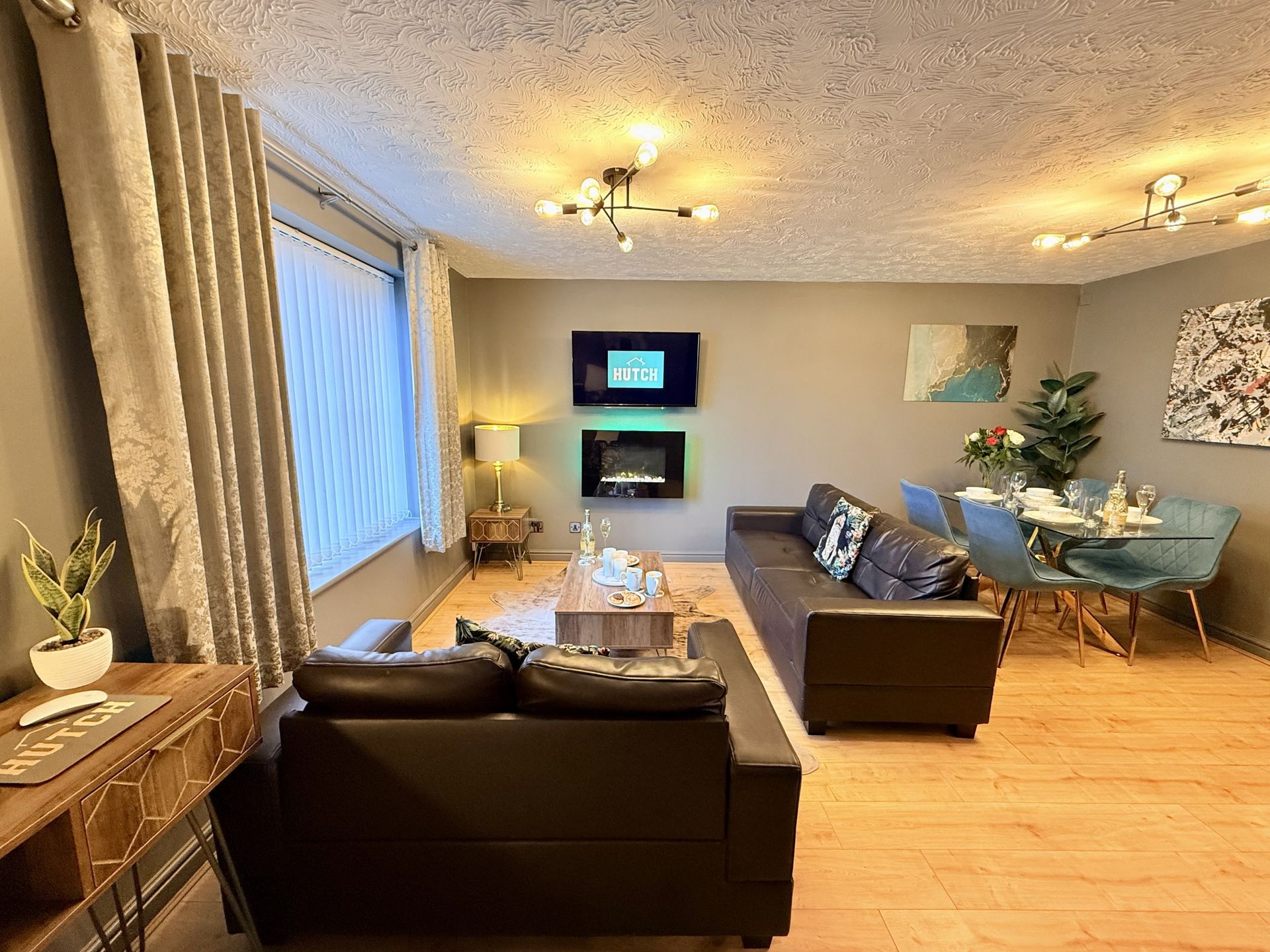 A modern living room with a brown sofa, a dining area, a fireplace, and a large window with grey drapes.