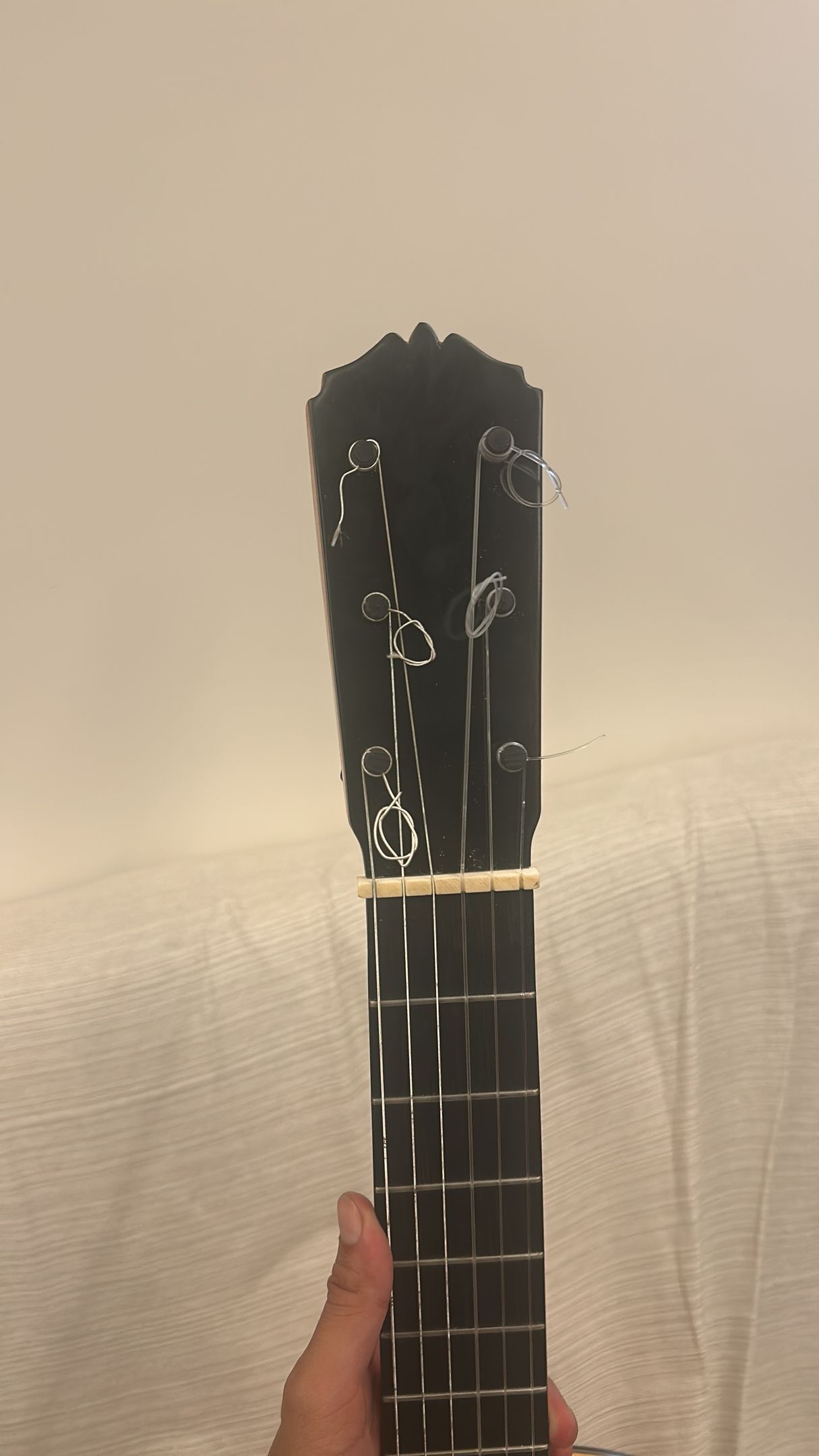 Una persona sostiene la pala negra y la parte superior del mástil de una guitarra sobre un fondo liso de color claro.