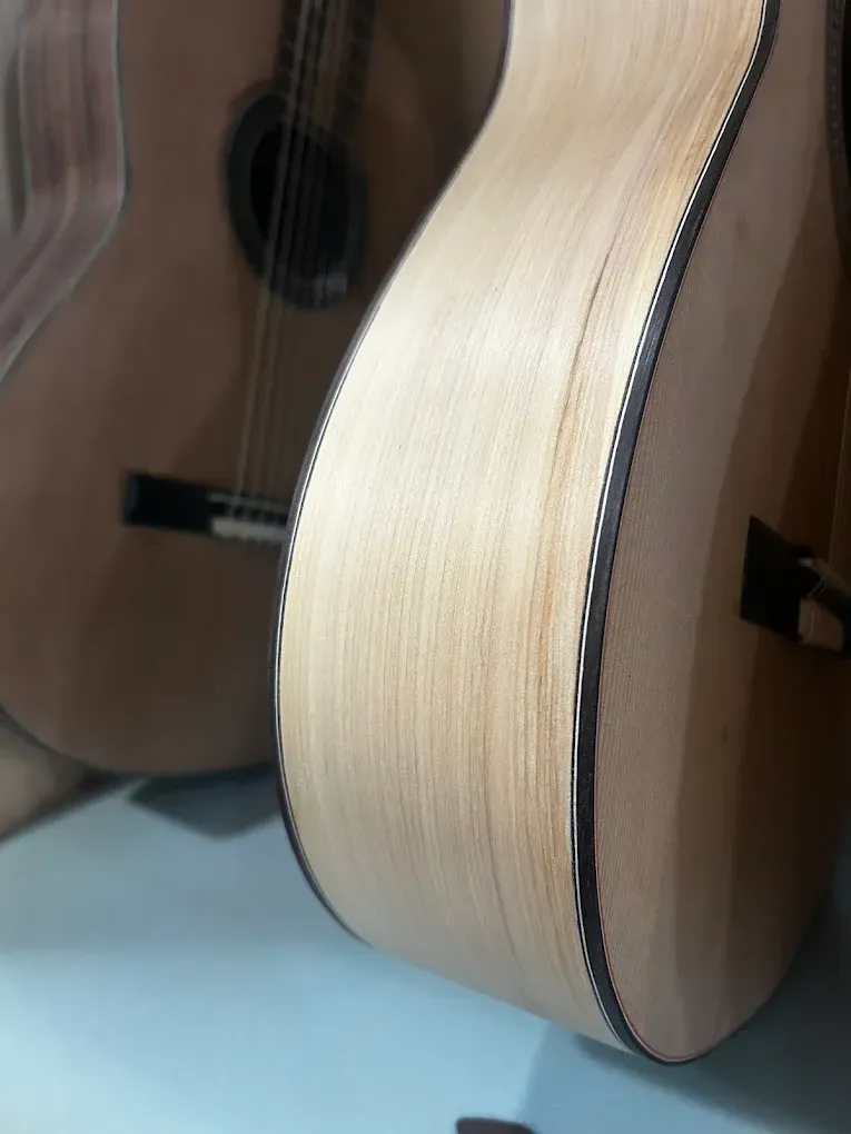 Vista lateral de dos guitarras acústicas de madera clara con ribete oscuro detallado sobre una superficie azul.