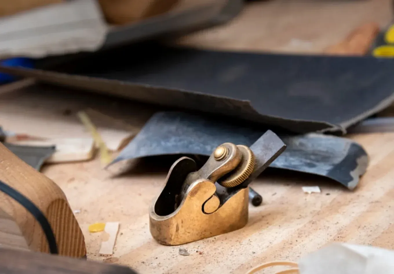 Un pequeño cepillo de carpintero de latón reposa sobre un banco de trabajo esparcido con papel de lija y restos de madera.