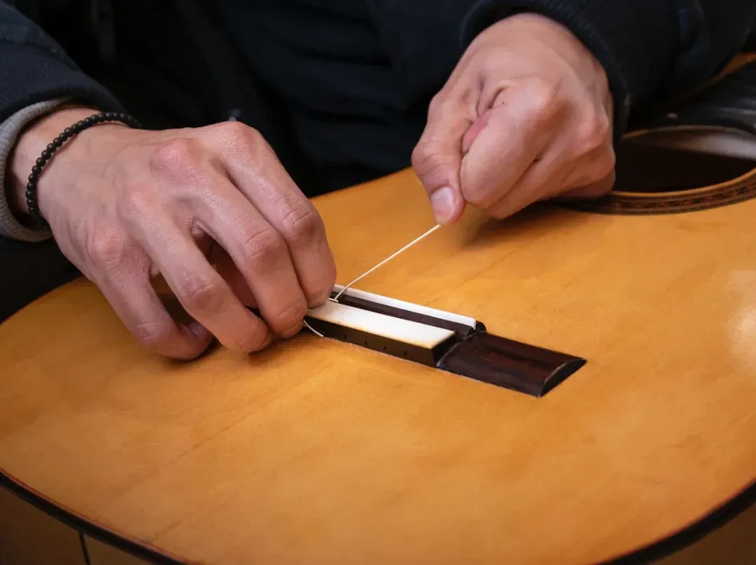 Primer plano de unas manos que pasan una cuerda de nailon a través del puente de una guitarra acústica de madera.