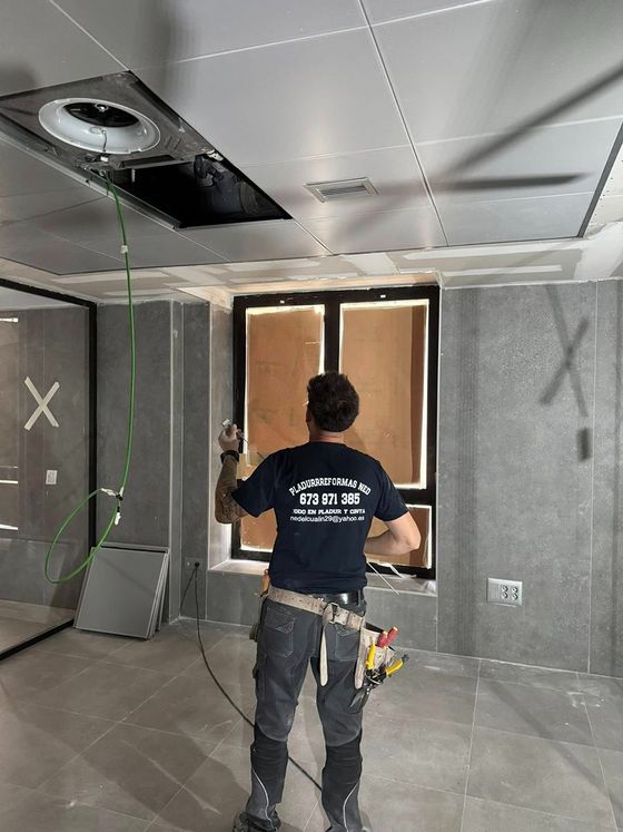 Hombre instalando ventilación en el techo de una habitación en construcción. Se ven cables verdes y herramientas.