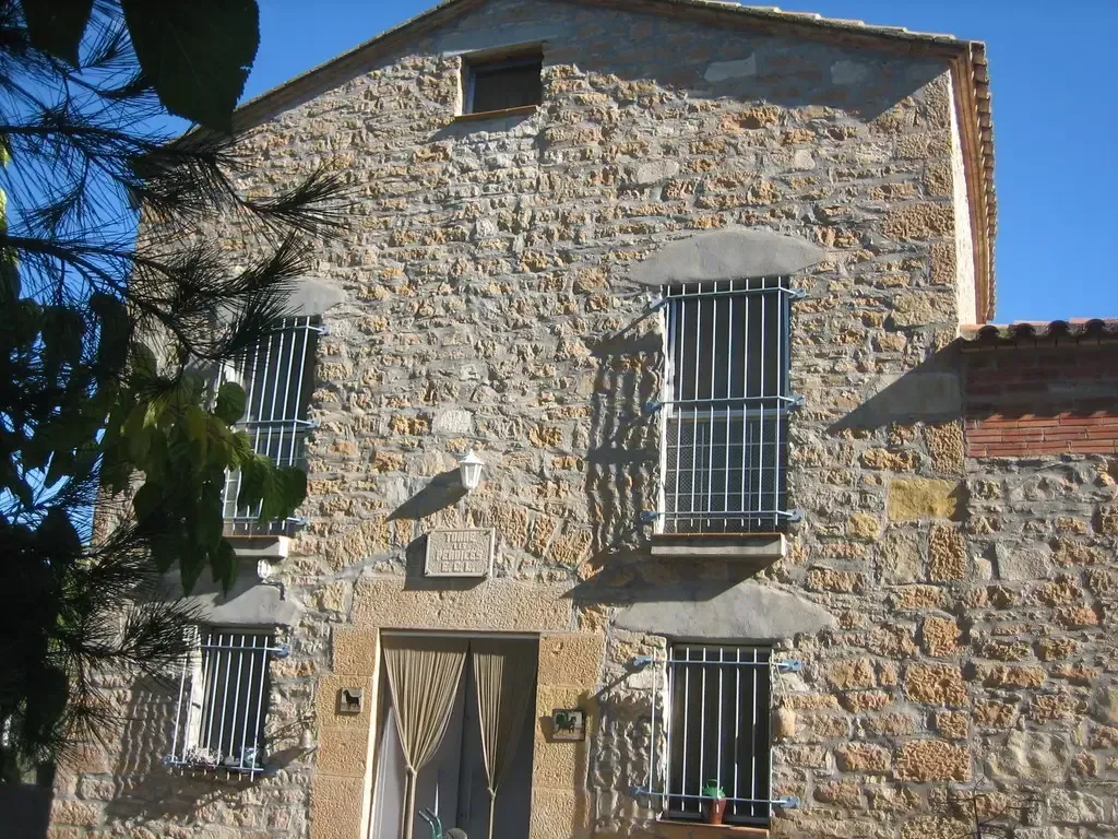 Edificio de piedra con ventanas enrejadas, puerta y pequeño balcón contra un cielo azul.