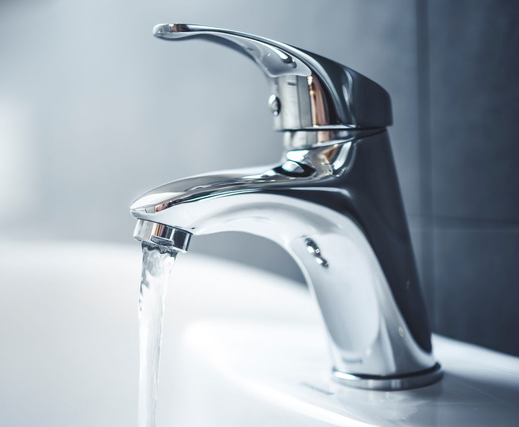 Un robinet de salle de bain chromé d'où l'eau coule du bec.
