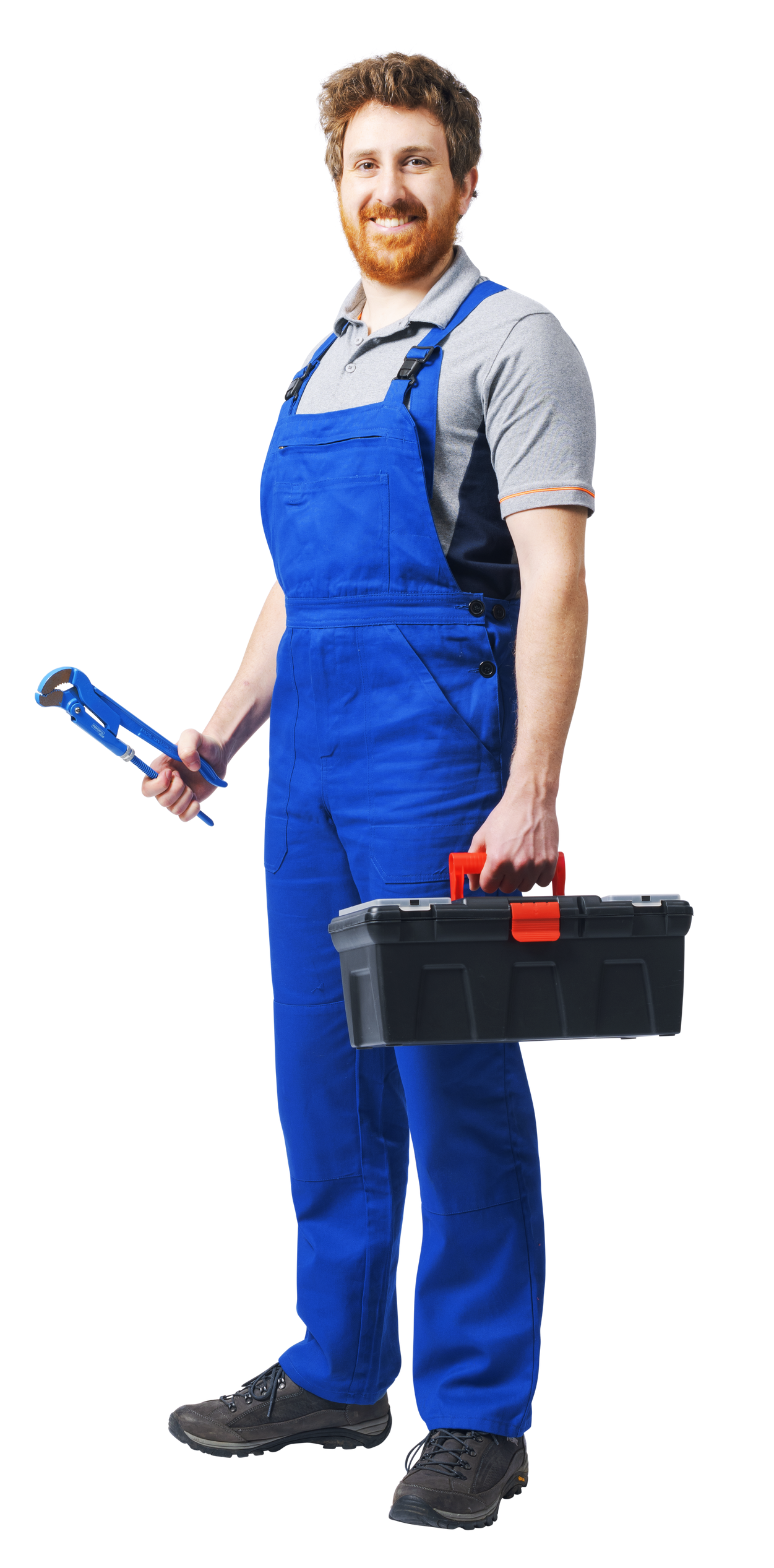 Un ouvrier souriant en salopette bleue tient une clé à pipe et une boîte à outils noire sur fond blanc.