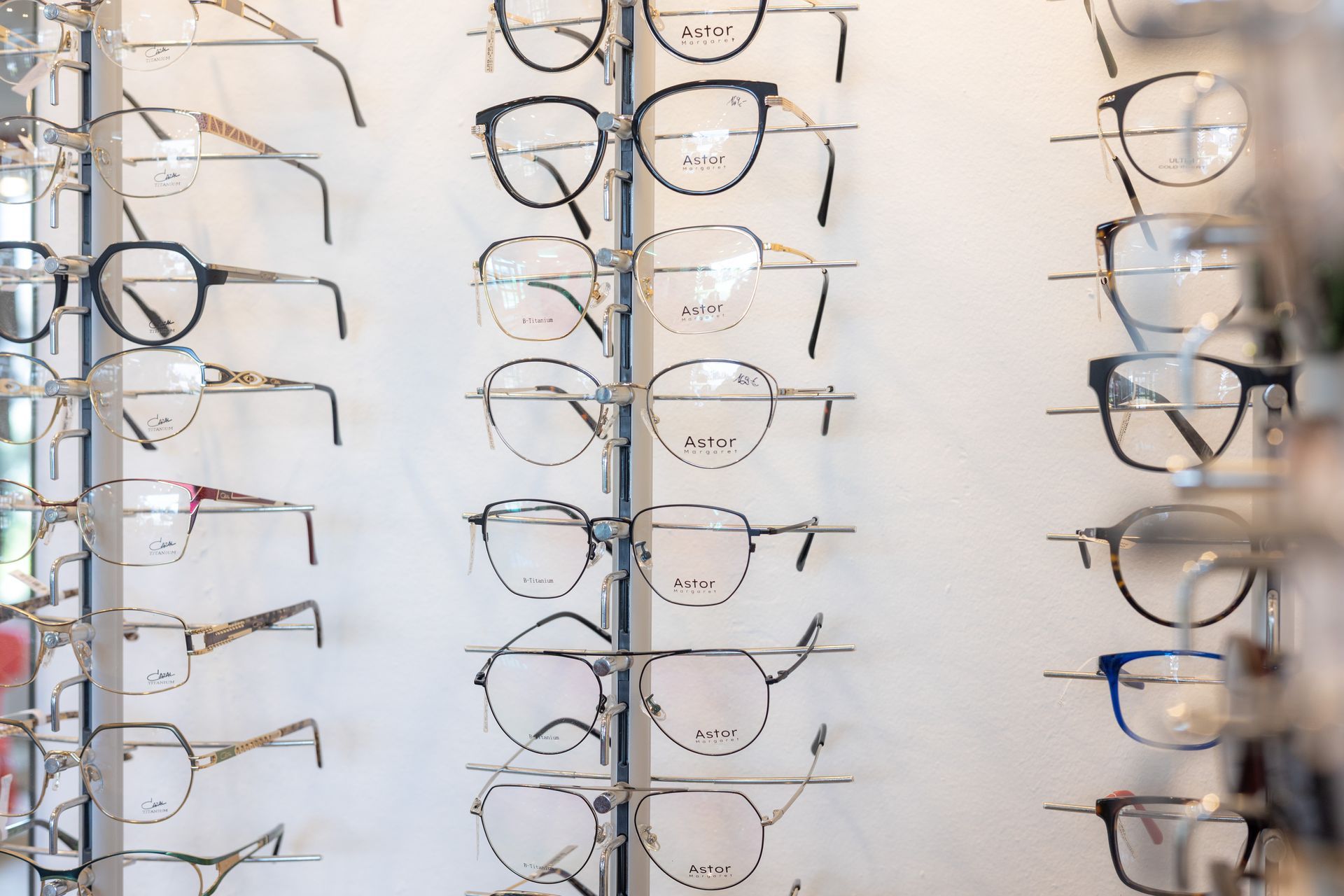 Brillen in einem Optikergeschäft. Verschiedene Rahmenstile und -farben an einer weißen Wand.