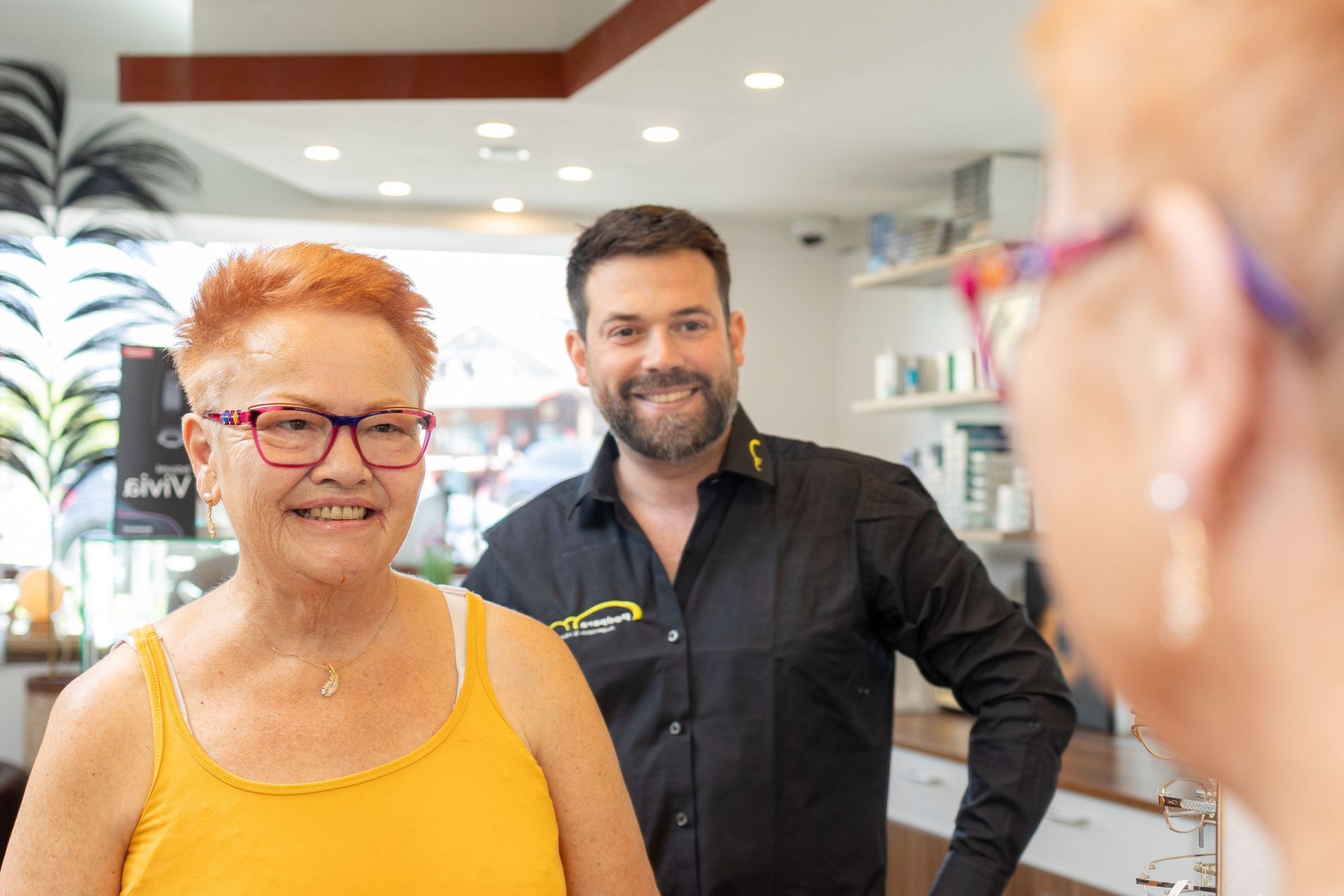 Frau probiert in einem Geschäft mit einem Optiker eine Brille an. Beide lächeln.