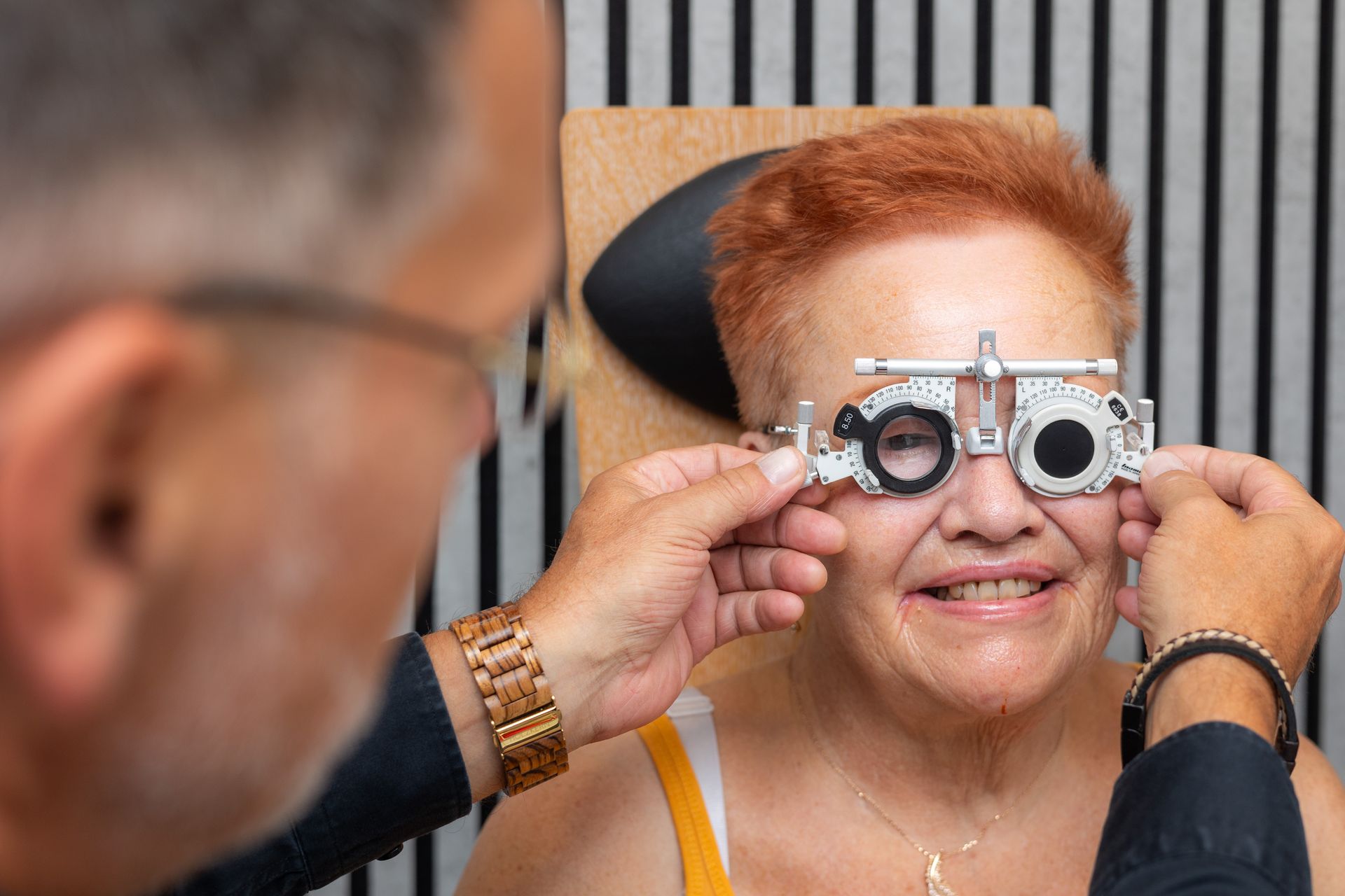 Optiker passt während einer Augenuntersuchung die Brille einer lächelnden älteren Frau an.