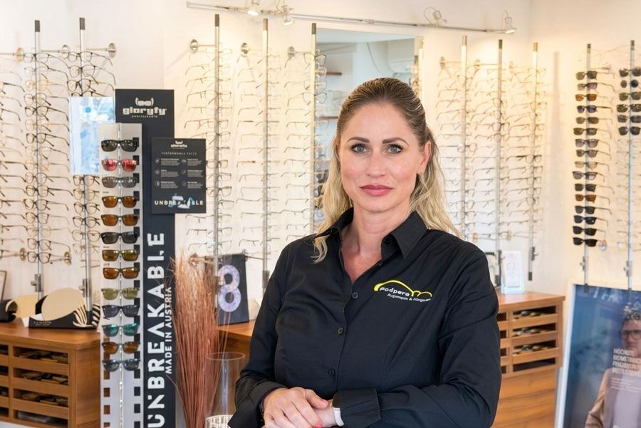 Eine Frau steht in einem Optikergeschäft neben einer Auslage mit Sonnenbrillen und Brillengestellen.