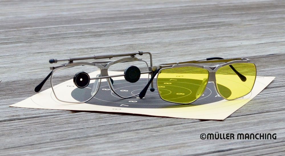 Zwei Schießbrillenpaare auf einer Papierscheibe, eines klar mit schwarzem Sichtfenster, das andere gelb getönt.