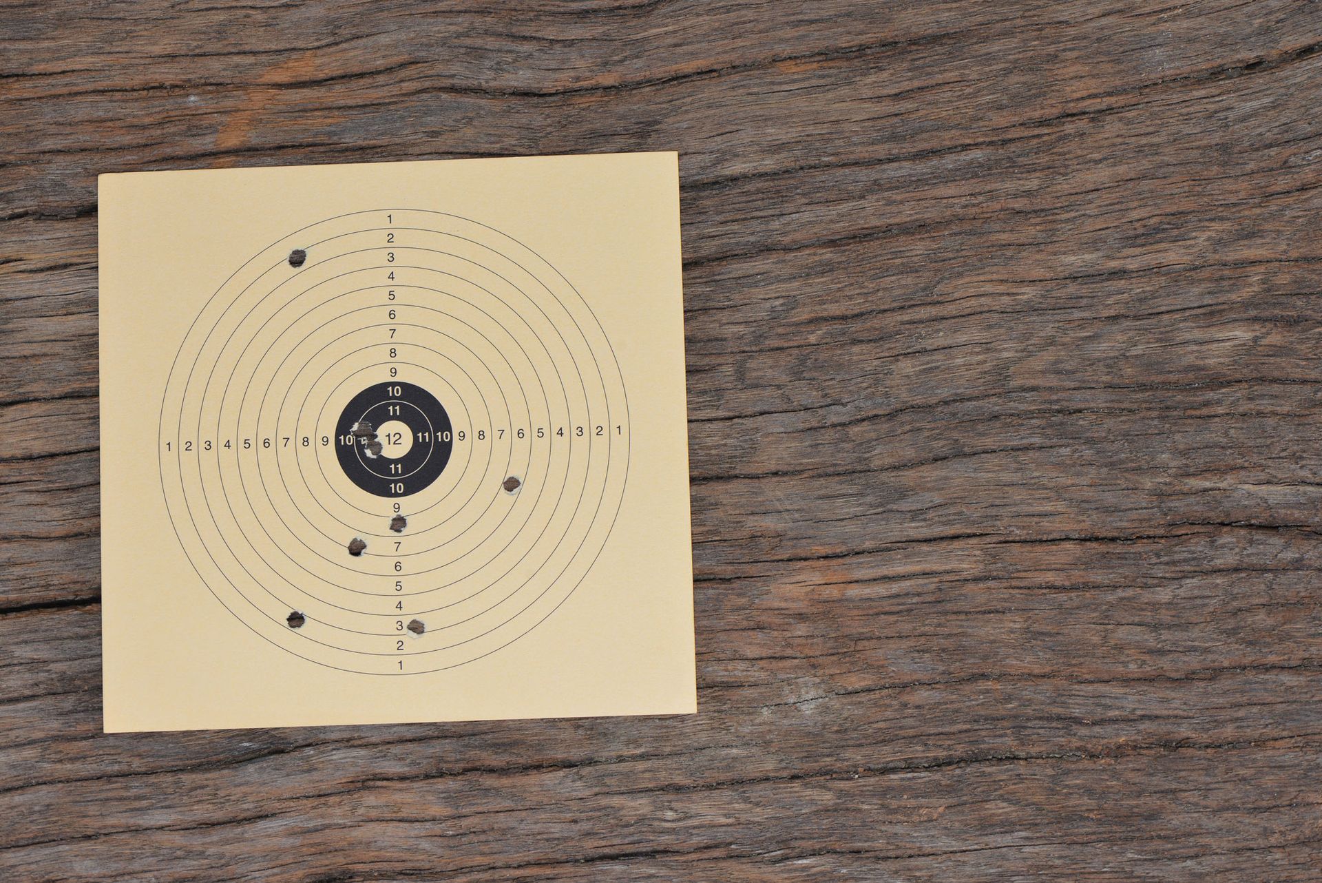 Auf einer Holzoberfläche befestigtes Zielübungspapier mit mehreren Einschusslöchern in der Mitte.