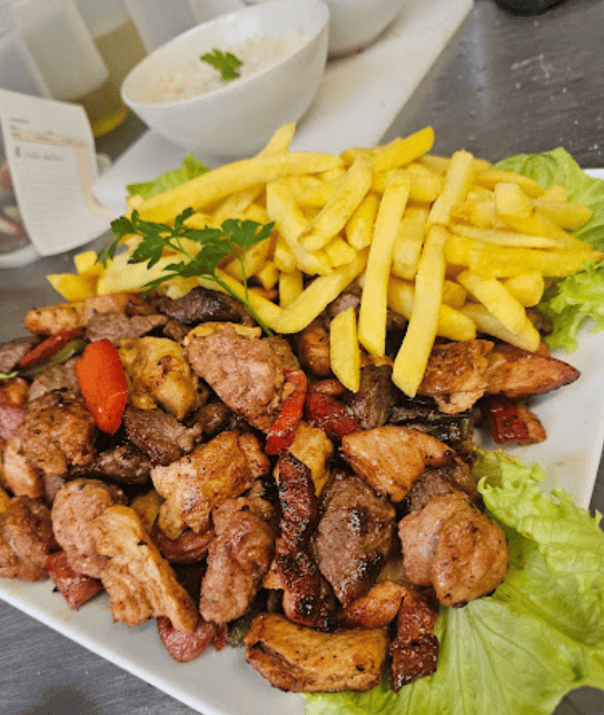 Un plato blanco cubierto con carne y papas fritas.
