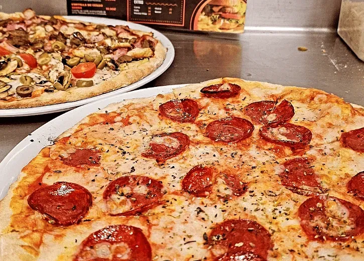 Hay dos pizzas sobre un mostrador, una al lado de la otra.