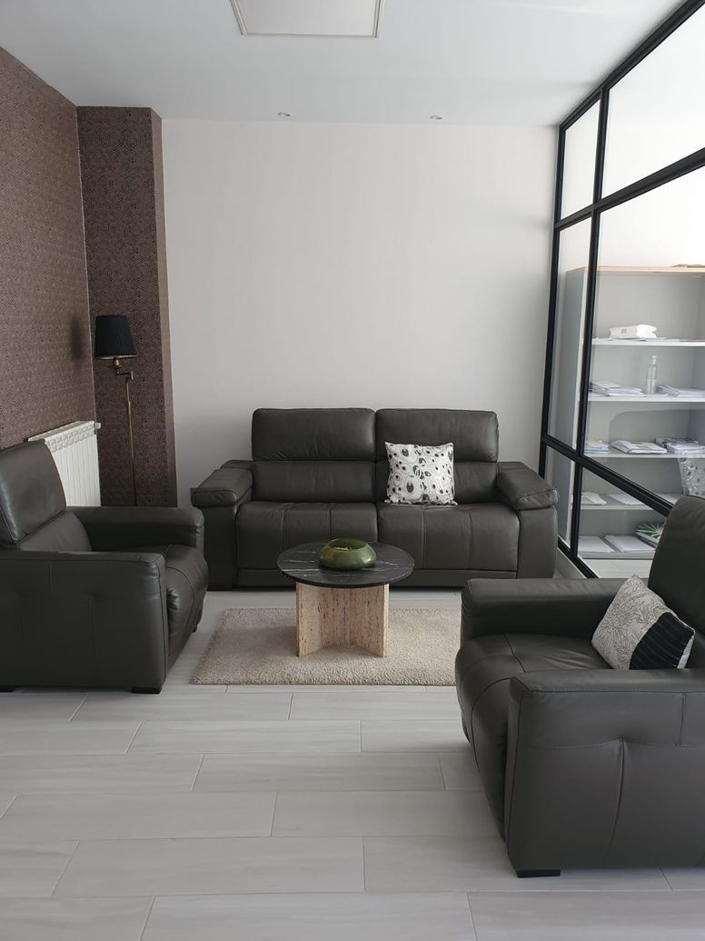 Sala de estar con sofá gris, sillones, mesa de centro, alfombra y pared decorativa.