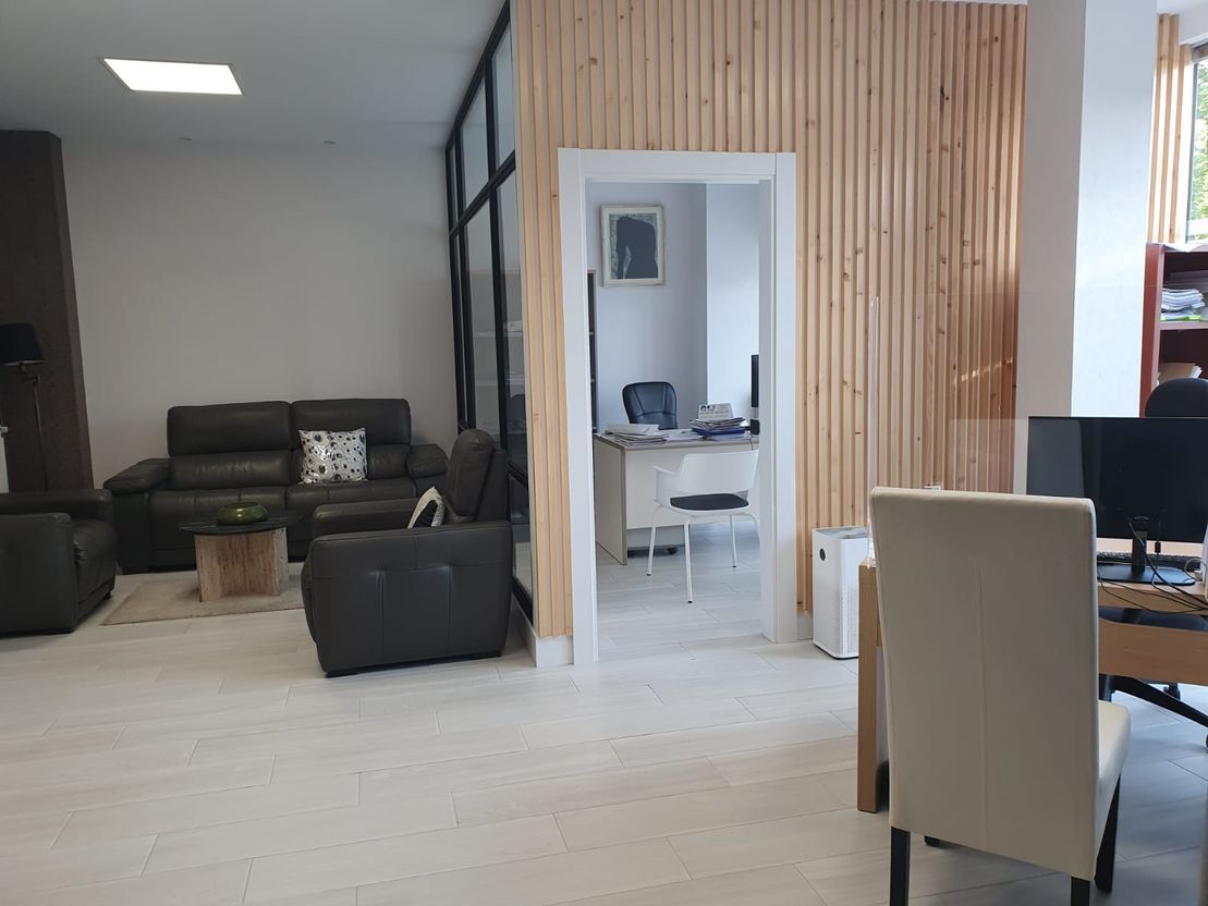 Interior de oficina con piso blanco, sofás marrones y una puerta que conduce a un espacio de oficina más pequeño.