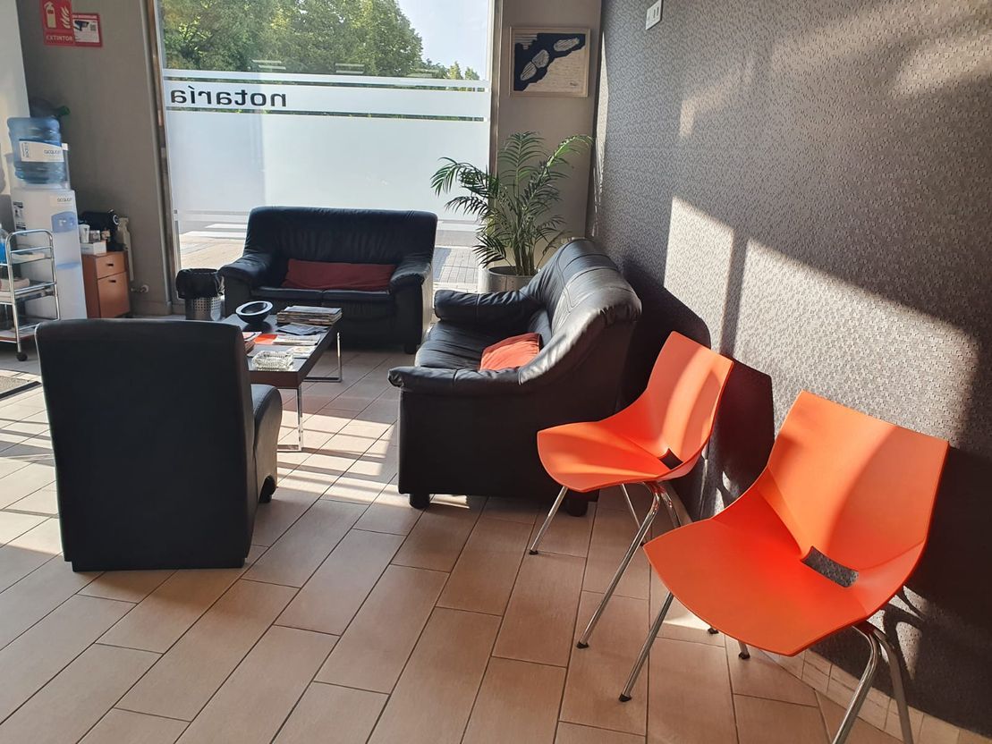 Sala de espera con sofás de cuero negro, sillas naranjas y una mesa.