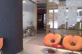 Sillas naranjas en un vestíbulo, junto a puertas de cristal con la inscripción 