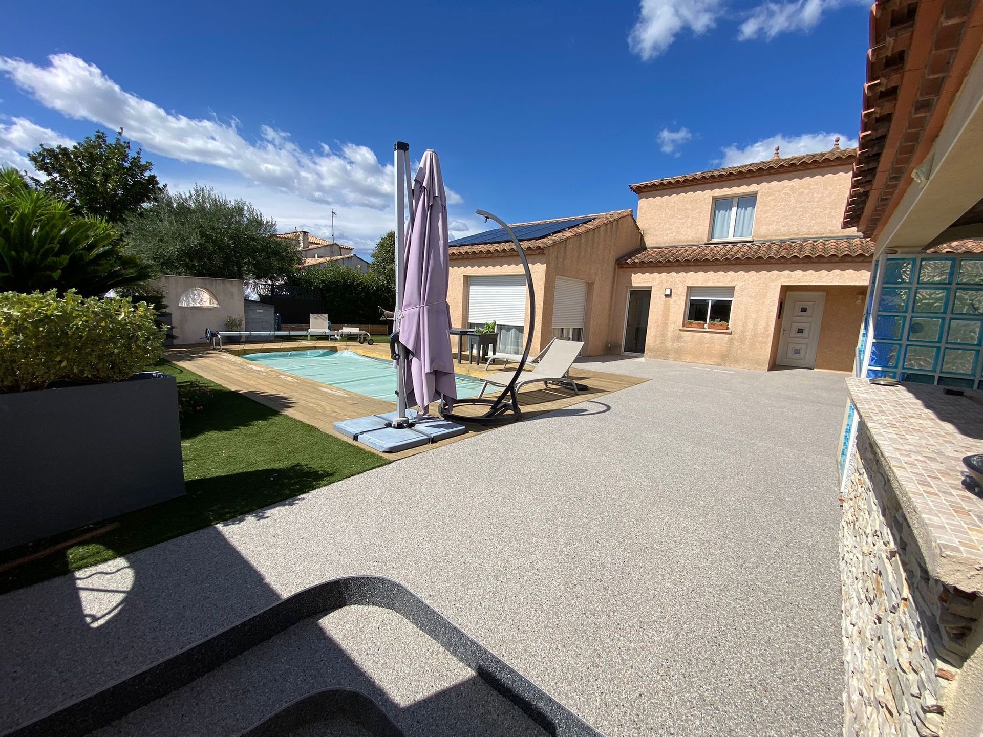 Terrasse extérieure spacieuse avec piscine et plage en résine, entourée de végétation.